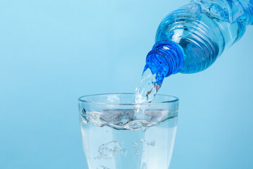 Water pouring from bottle into glass on color background