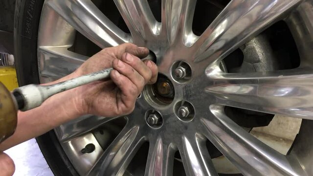 Mechanic drives in lug nuts onto rim of vehicle with dirty hands.  