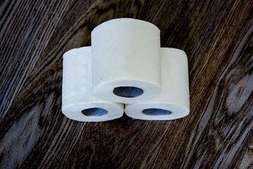 Three rolls of white toilet paper on a wooden background