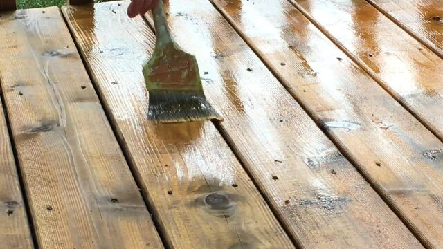 Elongated shot of brush staining deck with boards glistening with oil and two dry boards having stain applied to them.