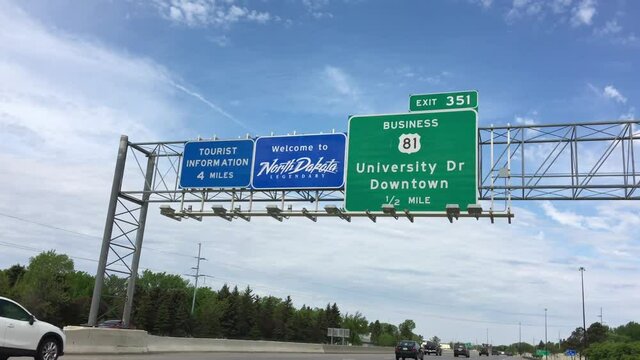 Blue welcome to North Dakota sign above highway on partly cloudy day.  