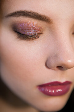 Vertical close-up of woman with bright makeup in mauve colors with eyes closed. Nude visage with perfect eyebrow shape and sparkle eyeshadow pigment