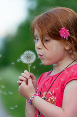 Red hair child blows on a flower