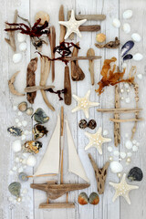 Abstract seaside collage with decorative sailing boat, driftwood, seashells, rocks, pearls and seaweed on distressed white wood background.