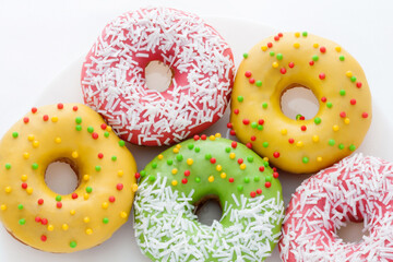 Yellow, green and pink Donuts with polka dots on a plate on a white background. National Doughnut Day. Dessert food. Fried dough confectionery. Snacks.