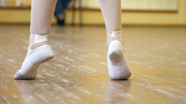 Close-up of a girl's legs in white ballet shoes on an old wooden floor during ballet training. Element of classical dance exercise.