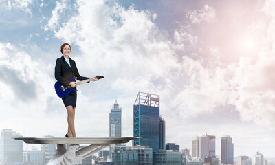 Attractive businesswoman on metal tray playing electric guitar against cityscape background