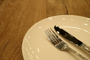 Off White Ceramic Plate with Silver Table Knife and Fork on the Wooden Table 