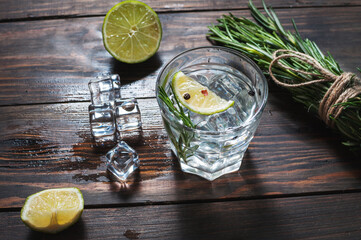 Alcoholic drink - gin tonic cocktail - with lime, rosemary and ice on rustic wooden table