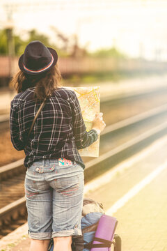 Traveler is waiting at the railway station. Travel concept. Woman sitting with map compass and travel bag at the train station. Traveler holding map and planing for next trip. Traveler reading map
