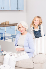 Granddaughter teaching her grandmother how to play on computer. Happy granny using laptop computer. Happy ladies smiling for camera.