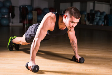Gym man push-up strength pushup exercise with dumbbell in a fitness workout