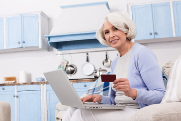 Elderly woman buying goods on Internet. Happy woman smiling for camera. Pretty lady showing credit card to photographer.