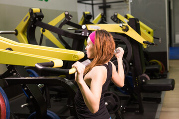 Sexy fitness girl exercising at the fitness gym. Make exercise with sports simulator.