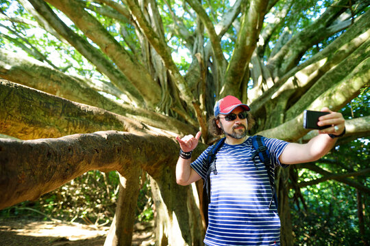 Male tourist taking photo of himself near giant banyan tree on Hawaii