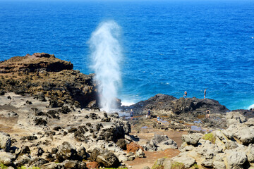 Tourists admiring the Nakalele blowhole on the Maui coastline. A jet of water and air is violently forced out through the hole in the rocks.