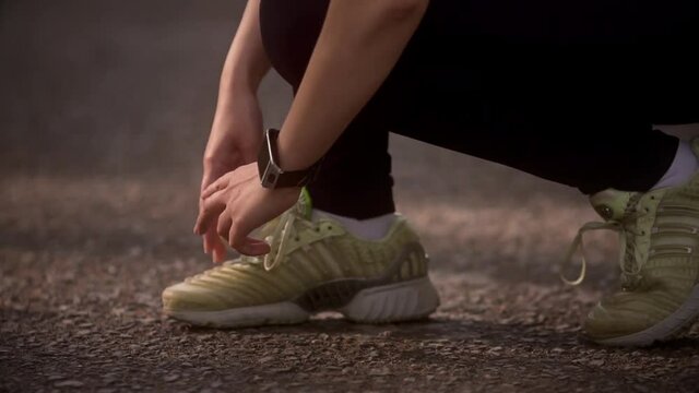 young woman ties up her sneakers and prepares for a jog. A girl with a smart watch is doing sports in the summer forest. slow motion