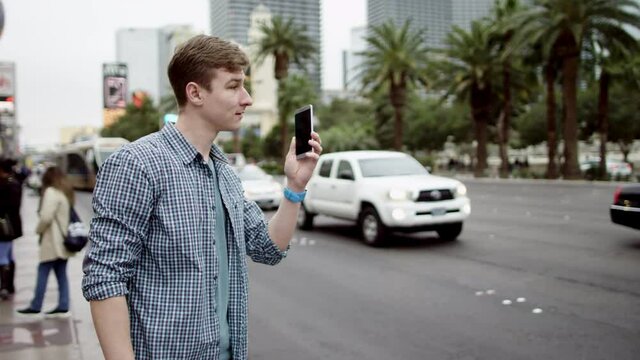 Young man is calling his friend on a street by using his smartphone