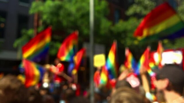 Rainbow flags flying on a float and in the hands of spectators on the sidelines of a summer gay pride parade in Greenwich Village, New York City