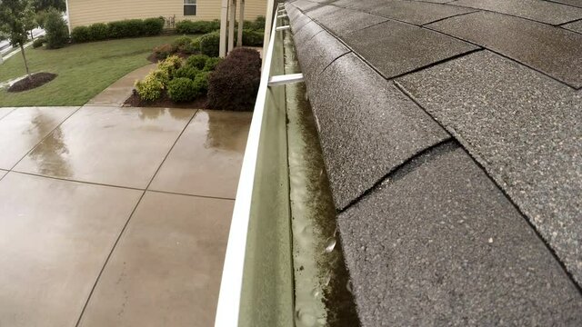 Rain falling into rain gutter from a shingle roof.