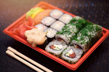 Japanese sushi in red plastic container for carrying food on black. Roll made of crab meat, avocado, cucumber inside and masago smelt roe outside.