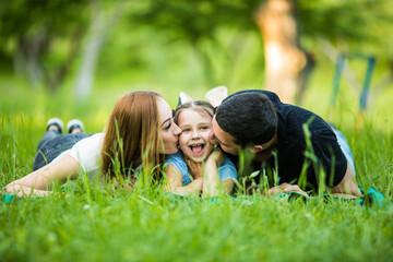 Parents with their daughter lying in summer park. Family lying on the green grass.