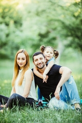 Young family mother father and daughter sitting on grass in park