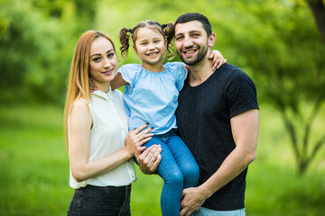 Happy young mother, father and daughter in summer park