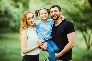 Happy young family spending time together in green nature. wife with husbend and daughter. Mother and father holding daughter in park