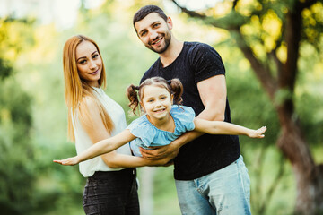 Fototapeta premium Happy young family play in summer park. Mother, father and daughter fly in the summer park.