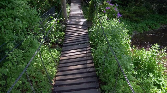 Pov come across small suspension footbridge new and modern tiny bridge over small creek in forest