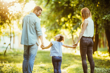 Happy family in the park. Mom, dad and baby happy walk at sunset. The concept of a happy family. Parents hold the baby's hands.