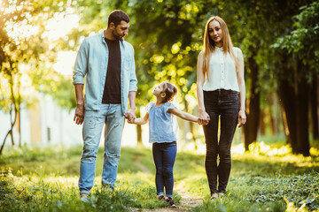 Obraz premium Mother, father and little girl walking in summer park and having fun