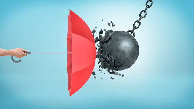 A Male Hand Holding An Open Red Umbrella Which Protects From A Collision With A Broken Wrecking Ball.