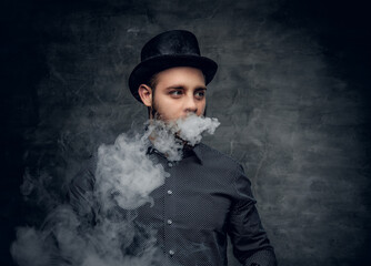 Bearded male smoking electronic cigarette over grey background.