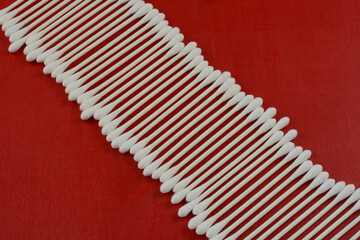 White cotton swabs in a line on red wood background