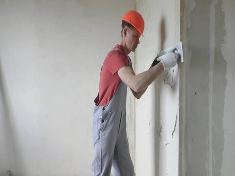 Worker is putting a gypsum plaster on a wall. He is using a long trowel.