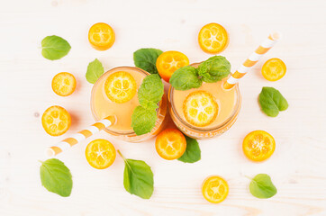 Freshly blended orange citrus kumquat  fruit smoothie in glass jars with straw, mint leaf, cute ripe berry, top view, close up. White wooden board background.