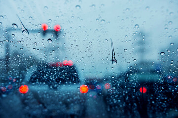 Blurred background of traffic jam on rainy day at crossroad junction street in Bangkok with many red light, Selective focus on rain drop, Dark blue tone - obrazy, fototapety, plakaty