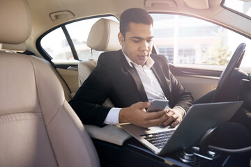 Serious businessman in a car with laptop