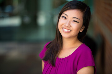 Cute pretty young youthful head shot of asian american woman with genuine natural smile bright colors