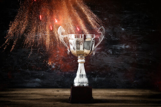 low key image of trophy over wooden table and dark background, with abstract fireworks.