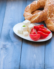 Traditional Turkish bagel (bread) - simit with tomatoes and feta cheese on a plate on a woodenbackground. Copy space and close up.