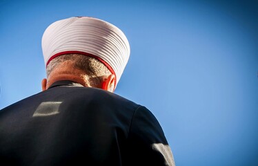 Muslim cleric seen from his back with a blue sky background. An editorial illustration for Ramadan fast, Muslim prayer, Islamic piety, interfaith dialogue, prayer to God, abstract  Ramadan concept.