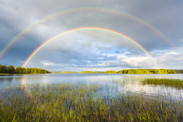 Fototapeta na wymiar Rainbow in midsummer over the lake in beautiful landscape in Finland