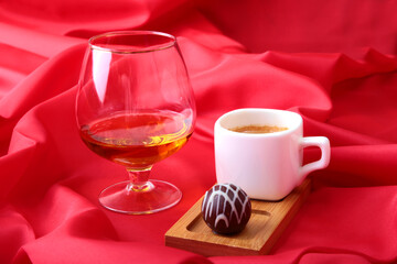 White cup of coffee and cognac in a glasses, pralines on red background.