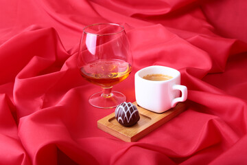 White cup of coffee and cognac in a glasses, pralines on red background.
