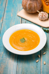  Top view of pumpkin and carrot soup with cream and parsley on blue  wooden background.