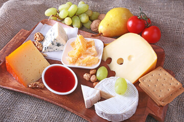 Assortment of cheese with fruits, grapes and nuts on a wooden serving tray.