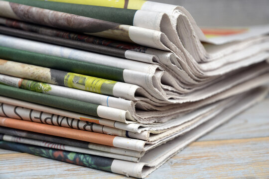 Stacked and piled up newspapers on a wooden table background
